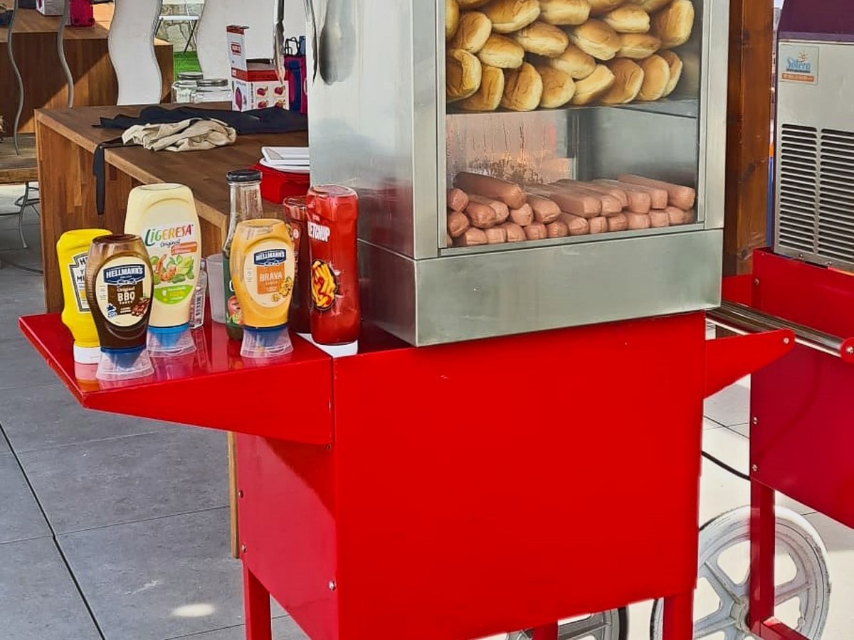 Carrito rojo de perritos calientes preparado con las salsas en un evento