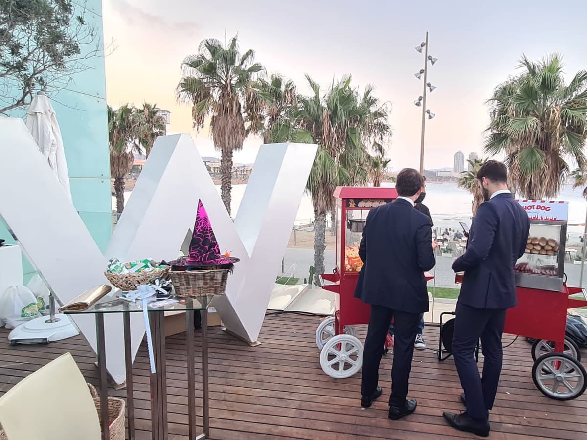 Invitados de traje junto al carrito de hotdogs en una terraza frente al mar
